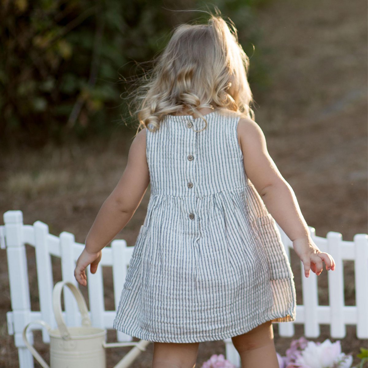 Baby trägt ärmelloses Musselin-Kleid aus Bio-Baumwolle in Grau (OrganicEra) läuft aus dem Bild man sieht die Rückseite des Kleides