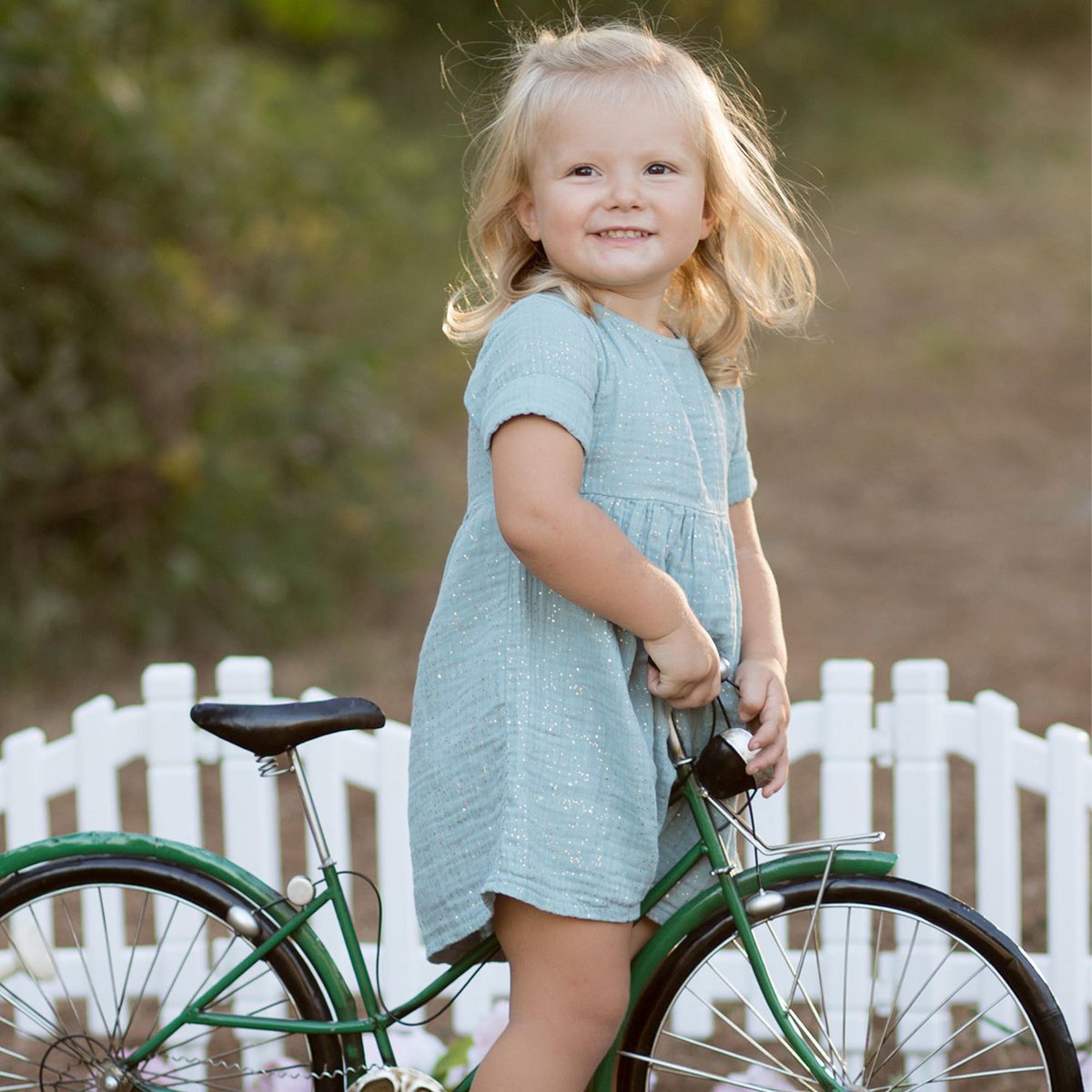 Kinderkleid aus Bio-Musselin in Aqua mit Glitzer wird von Kleinkind getragen auf einem Fahrrad