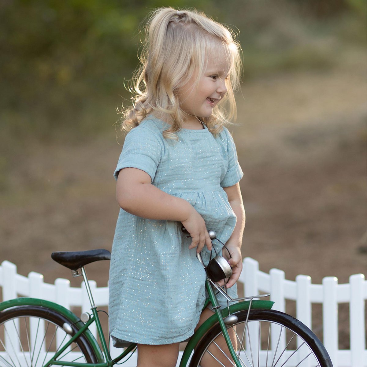 Kinderkleid aus Bio-Musselin in Aqua mit Glitzer getragen von blondem Mädchen auf einem Fahrrad